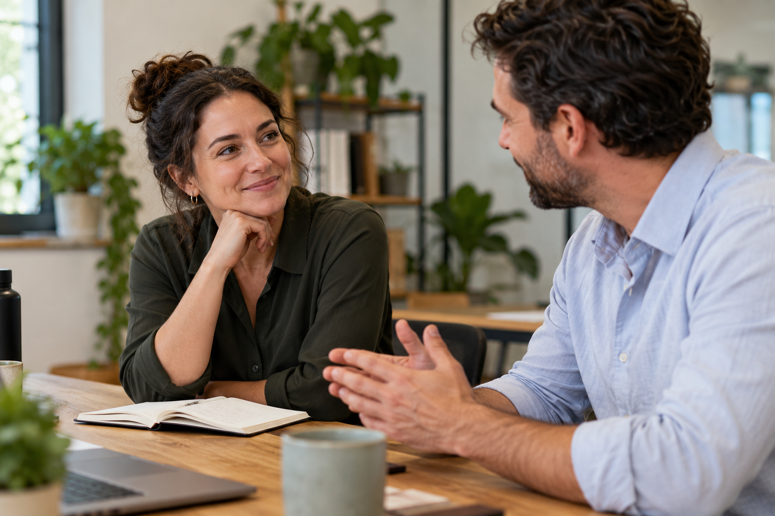 Two colleagues having a relaxed conversation at a workplace table.